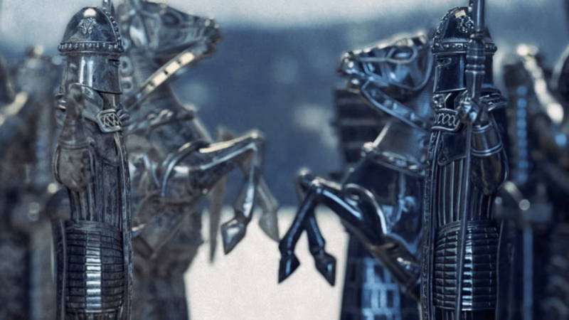 Be Ekhtesar close-up of opposing metallic chess pieces shaped as armoured figures and rearing horses.