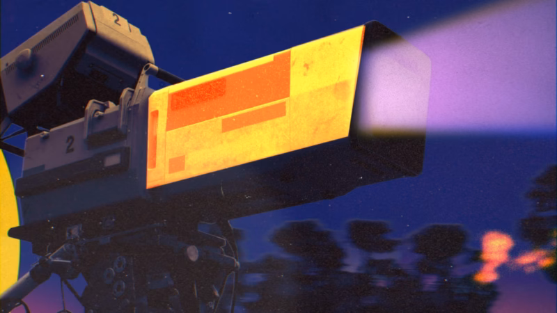 Television studio camera with yellow and orange panels and a purple light beam against a dark blue background.