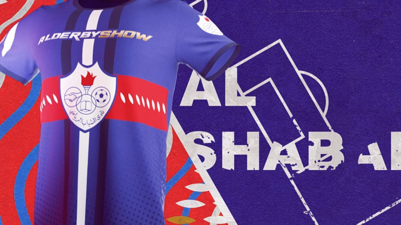 Close-up of a blue Al-Shabab football shirt with a red chest band and club crest beside outlined number 1 graphics.