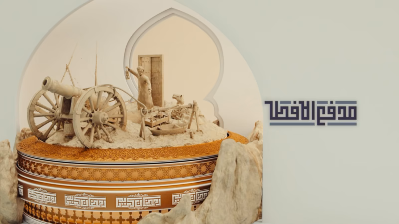Madfa’ Al-Iftar — a cannon, dhow and lantern-bearing figure on an ornate golden platform beside the Arabic programme title
